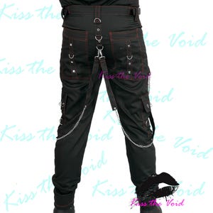 May include: Black pants with red stitching, cargo pockets, and silver chain accents. The pants feature metal studs and a suspender-style strap. The text "Kiss the Void" is visible in the background.