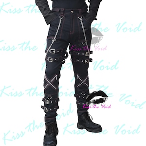 May include: Black denim trousers with red stitching, multiple straps with buckles, silver chains, and zip detailing. The trousers have a distinctive, edgy design, suitable for alternative fashion.