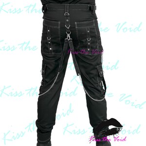 May include: Black cargo pants with white stitching, metal studs, and chain detailing. The pants have multiple pockets and a strap with metal rings. The text "Kiss the Void" is visible in the background.
