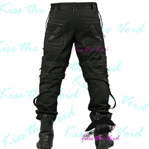 May include: Black cargo pants with multiple pockets, straps, and zippers. The pants have a unique design with reinforced stitching and metal accents. The pants are paired with black boots. The text "Kiss the Void" is visible in the background.
