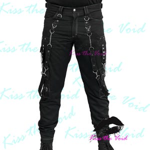 May include: Black pants with white stitching, featuring multiple straps, chains, and metal hardware. The pants have pockets and decorative elements, creating a unique, edgy style. The text "Kiss the Void" is visible in the background.