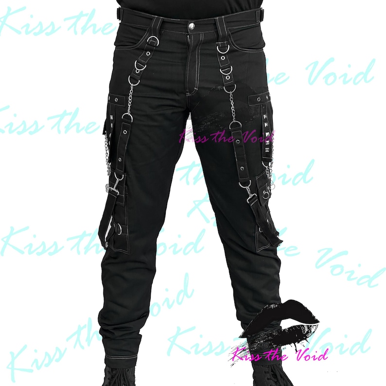 May include: Black pants with white stitching, featuring multiple straps, chains, and metal hardware. The pants have pockets and decorative elements, creating a unique, edgy style. The text "Kiss the Void" is visible in the background.