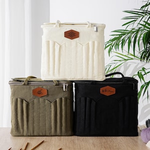 May include: Three square storage bags for yarn and knitting supplies in cream, olive green, and black. Each bag features a zippered top, two carrying handles, and a front panel with vertical pockets and a brown leather-like patch with text.