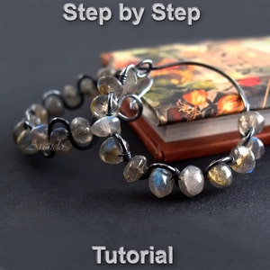 May include: Step-by-step tutorial for making earrings with labradorite stones and black wire. The earrings are hoop-shaped and feature a wavy wire design.
