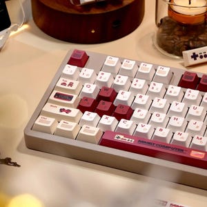 May include: A white and cream keyboard with red and pink keys. The keyboard has a Japanese layout and the text "FAMILY COMPUTER" is printed on the space bar.