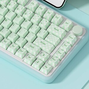 May include: A light green and white keyboard with a checkered pattern on the keys. The keyboard has a light blue frame and a light blue background.