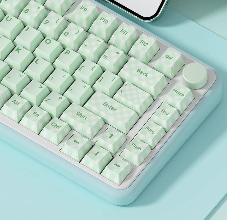 May include: A light green and white keyboard with a checkered pattern on the keys. The keyboard has a light blue frame and a light blue background.