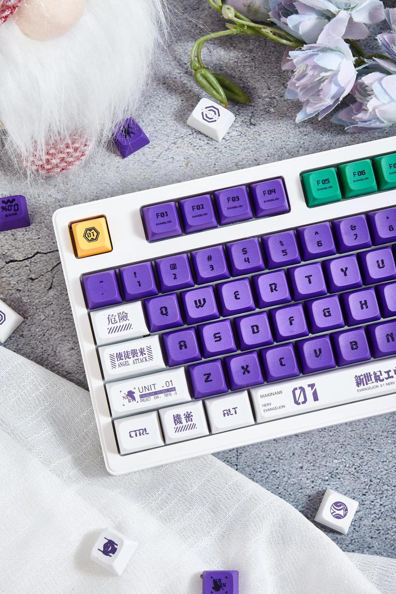 May include: A white keyboard with purple keys and white keycaps. The keycaps have Japanese and English text, including "Angel Attack" and "Unit 01".