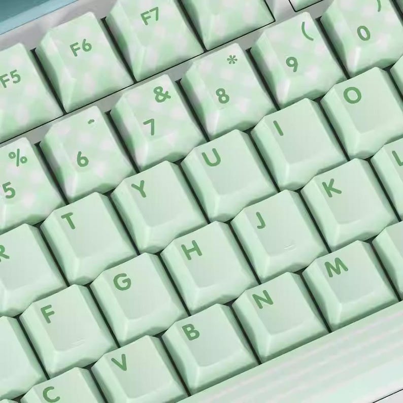 May include: A mint green keyboard with white lettering. The keys are labeled with letters, numbers, and symbols. The keyboard has a light green and white marbled design.