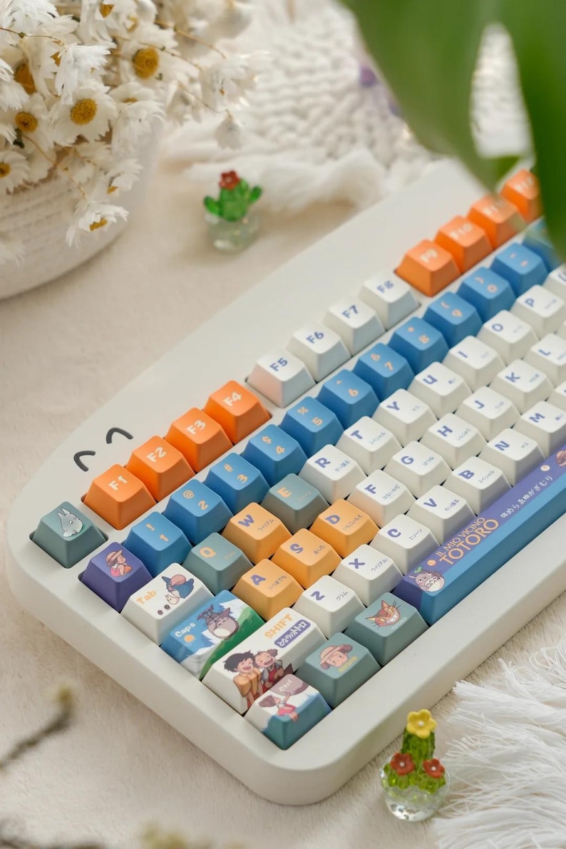 May include: A white keyboard with blue, orange, and yellow keys. The keys have illustrations of characters from the movie My Neighbor Totoro. The keyboard has a blue and white space bar with the text "My Neighbor Totoro" in Japanese.