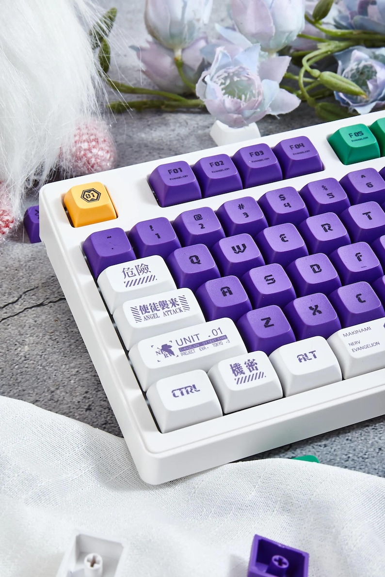 May include: A white keyboard with purple keycaps and white keycaps with Japanese text. The keyboard has a white frame and a white base. The keyboard is on a white surface with a purple and green flower in the background.