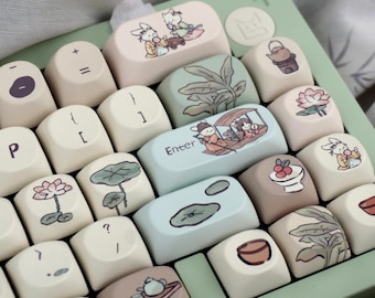 Puede incluir: Un teclado verde y crema con teclas personalizadas que presentan ilustraciones de flores, hojas y animales. Las teclas están hechas de un plástico blanco liso y tienen un acabado mate. El teclado tiene un diseño estándar con una fila de números, una fila de funciones y un área de teclado principal. Las teclas están dispuestas en un diseño escalonado, con las teclas más grandes en la fila inferior y las teclas más pequeñas en la fila superior. El teclado está conectado a una computadora a través de un cable USB.