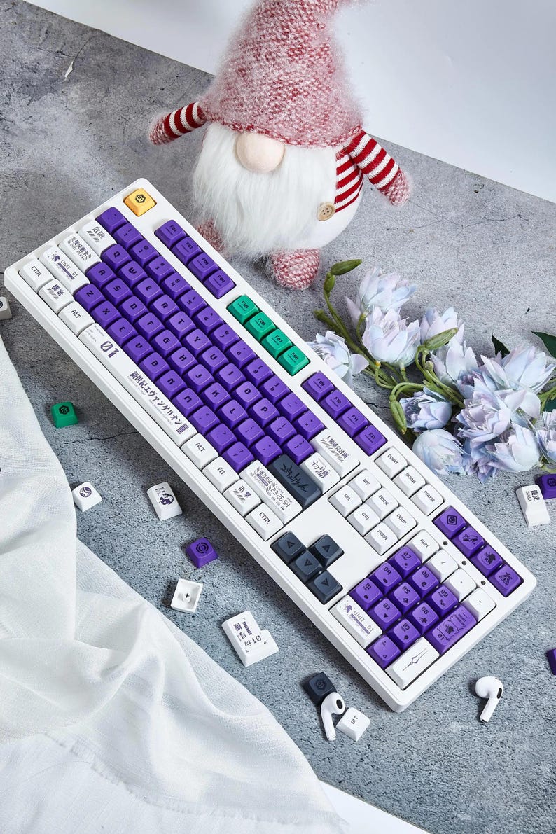 May include: A white mechanical keyboard with purple and green keycaps. The keyboard has a Japanese inscription that reads "新世紀エヴァンゲリオン" which translates to "Neon Genesis Evangelion".