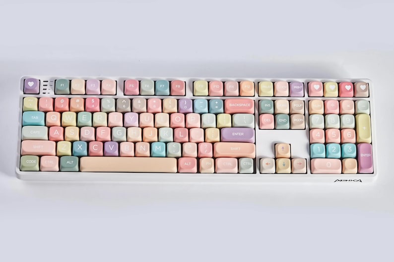 May include: A pastel-colored keyboard with white lettering on the keys. The keys are arranged in a standard QWERTY layout. The keyboard has a white frame and a light pink space bar.