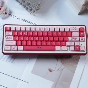 May include: A red and pink mechanical keyboard with custom keycaps. The keycaps feature cartoon character designs and the word "Kirby". The keyboard has a red frame and a white base.
