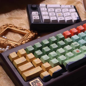 May include: Two mechanical keyboards with custom keycaps. One is black with white keycaps and a numeric keypad. The other has green, yellow, and orange keycaps with various designs and text.