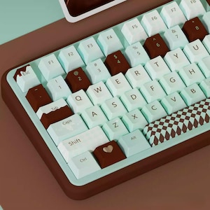 May include: A mint green and brown mechanical keyboard with a checkered keycap. The keyboard has a variety of keys, including Esc, F1-F8, Tab, Caps Lock, Shift, Ctrl, Alt, Q-Z, and numbers 1-8. The keyboard is on a brown surface.