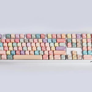 May include: A white keyboard with pastel colored keys. The keys have various letters, numbers, and symbols printed on them. The keyboard has the word "ARIKA" printed on the bottom right corner.