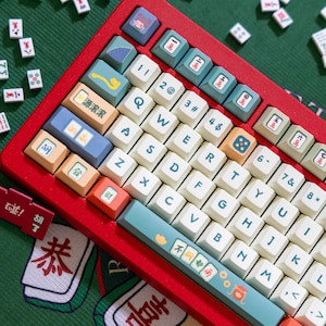Op de afbeelding: Een rood mechanisch toetsenbord met witte toetsen en aangepaste toetsen met Chinese karakters en illustraties. Het toetsenbord heeft een rood frame en een witte en blauwe toetsenset. De toetsen hebben een verscheidenheid aan ontwerpen, waaronder een Chinees karakter voor "geluk", een Chinees karakter voor "rijkdom" en een Chinees karakter voor "geluk".