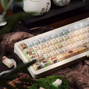 Pode incluir: Um teclado personalizado com teclas ilustradas. As teclas apresentam vários desenhos, incluindo personagens de desenhos animados e padrões. O teclado está sobre um fundo escuro.