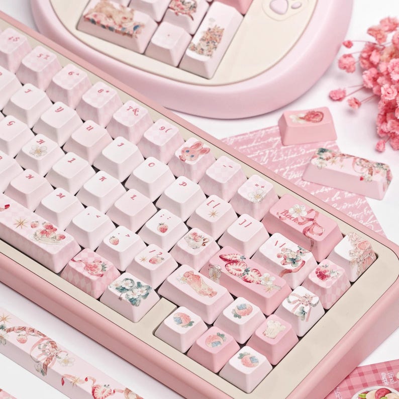 May include: A pink mechanical keyboard with custom keycaps featuring a variety of pastel-colored designs, including strawberries, flowers, and ribbons. The keycaps are labeled with letters and numbers, and the keyboard has a pink frame.