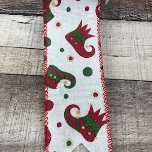 May include: White ribbon with a red border and a repeating pattern of green and red elf shoes with gold accents and red and green polka dots.