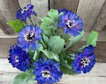 May include: A bouquet of blue artificial flowers with green leaves. The flowers have a white center and are arranged in a cluster.
