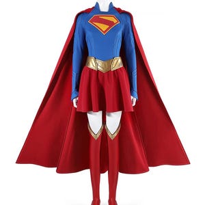 May include: A Supergirl costume featuring a blue long-sleeve top with a red and gold emblem, a red skirt, and a gold belt. The costume includes a red cape, red boots, and matching red leggings. The costume is displayed on a mannequin.