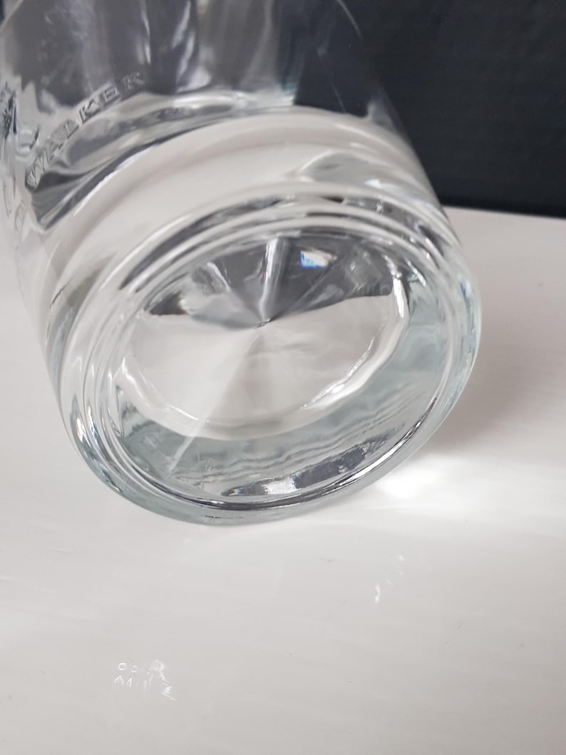 K&ouml;nnte beinhalten: Klares Trinkglas mit dickem Boden. Das Glas hat eine leichte Kr&uuml;mmung und einen abgerundeten Boden. Das Wort "WALKER" ist auf der Seite des Glases zu sehen. Das Glas steht auf einer wei&szlig;en Oberfl&auml;che.