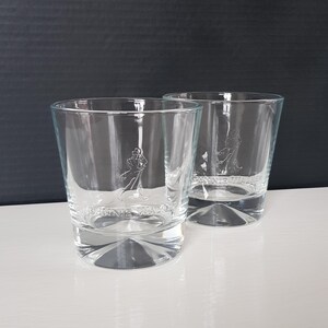 K&ouml;nnte beinhalten: Zwei klare, kurze Whiskygl&auml;ser. Jedes Glas hat ein Logo eines Mannes mit Gehstock und die Worte "JOHNNIE WALKER" auf der Vorderseite eingraviert. Die Gl&auml;ser stehen auf einer wei&szlig;en Oberfl&auml;che mit dunklem Hintergrund.