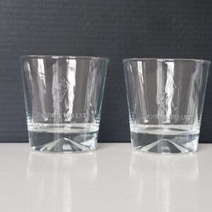 K&ouml;nnte beinhalten: Zwei klare Whiskeygl&auml;ser mit dem eingravierten "Johnnie Walker"-Logo auf der Vorderseite. Die Gl&auml;ser sind zylindrisch mit leicht ausgestellter Oberseite und stehen auf einer wei&szlig;en Oberfl&auml;che vor einem dunklen Hintergrund.