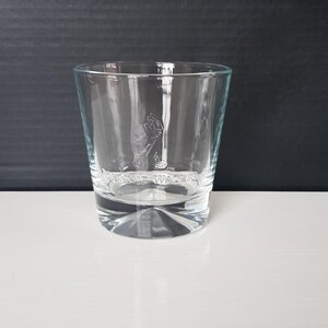 K&ouml;nnte beinhalten: Ein klares, kurzes Trinkglas mit dickem Boden. Das Glas zeigt ein ge&auml;tztes Bild eines Mannes, der geht, und die Worte "JOHNNIE WALKER" darunter. Das Glas steht auf einer wei&szlig;en Oberfl&auml;che und einem dunklen Hintergrund.