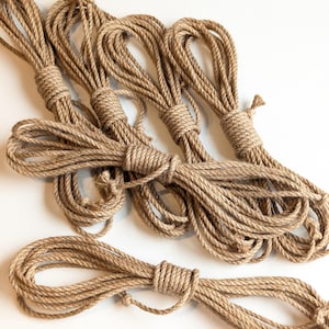May include: Several bundles of natural-colored rope, tightly wound and knotted. The rope appears to be made of a coarse, fibrous material, and is arranged against a white background. The bundles are of varying sizes, suggesting they are for crafting or decorative purposes.