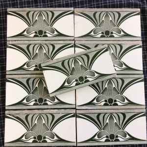 May include: Eight white ceramic tiles with a repeating Art Nouveau floral design in green and grey. The tiles are arranged in a grid, with one tile slightly offset, showing the pattern's continuity. The tiles have a decorative border, suitable for a kitchen or bathroom.