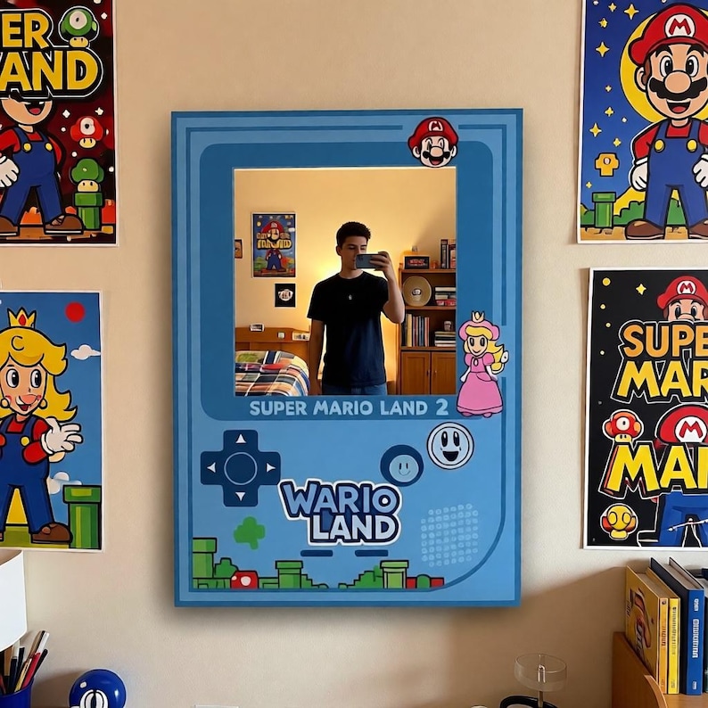 May include: A blue mirror in the shape of a Super Mario Land 2 Game Boy. The mirror has a rectangular shape with rounded corners and features Mario and Princess Peach stickers. The words "Super Mario Land 2" and "Wario Land" are printed on the mirror.