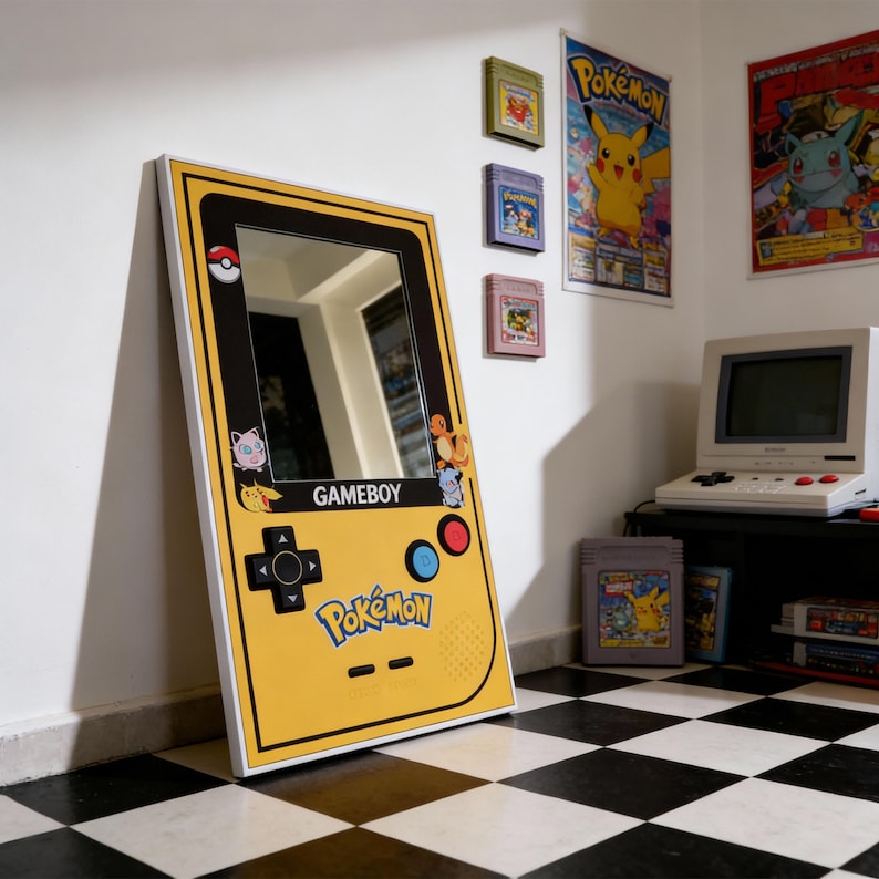 Puede incluir: Un espejo amarillo con forma de Gameboy con borde negro y marco blanco. El espejo presenta el logotipo de Pokemon e ilustraciones de personajes. El dise&ntilde;o incluye una cruceta, botones y la palabra "GAMEBOY".