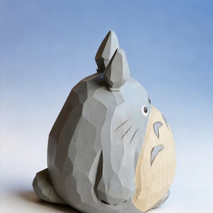 May include: A gray wooden sculpture of a cartoon character with large ears and a round body. The figure has a light beige belly and a small, black eye. The sculpture is carved with visible wood grain.