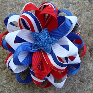 May include: A red, white, and blue ribbon bow with a sparkly blue star in the center. The bow is made of multiple layers of ribbon and is tied in a knot.