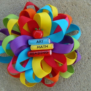 May include: A colorful rainbow ribbon bow with a red apple and three books with the words "ART", "MATH", and "READING" on them.