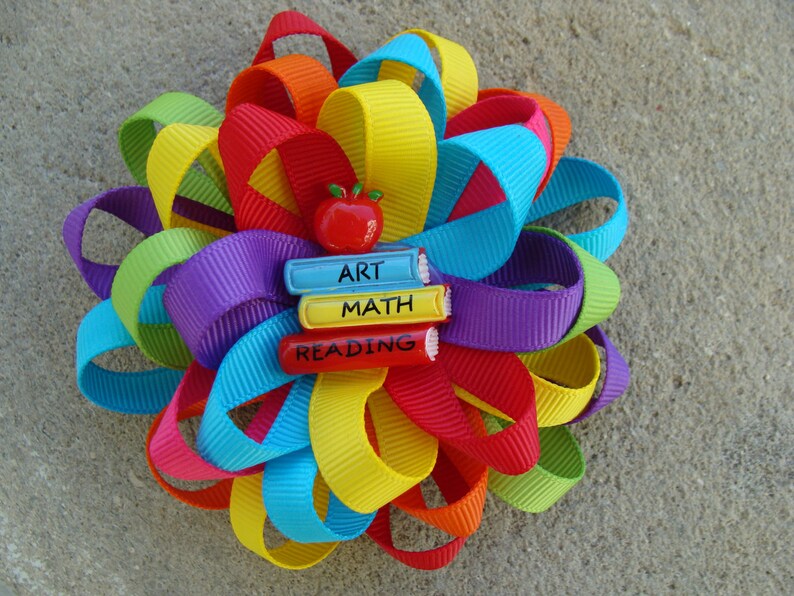 May include: A colorful rainbow ribbon bow with a red apple and three books with the words "ART", "MATH", and "READING" on them.