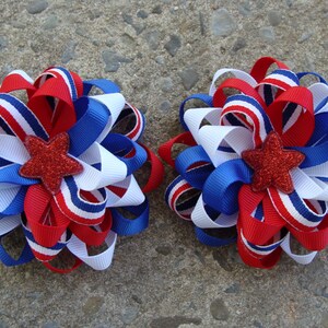 May include: Two red, white, and blue ribbon hair bows with a red glitter star in the center.