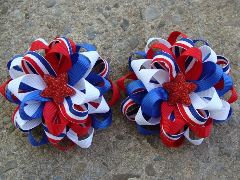 May include: Two red, white, and blue ribbon hair bows with a red glitter star in the center.