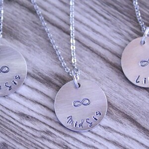 May include: Three silver necklaces with infinity symbol charms and the words "Big Sis", "Mid Sis", and "Lil Sis" engraved on the charms.