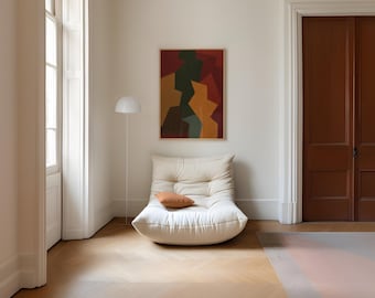May include: A cream-colored, low-profile lounge chair with a small, orange pillow. A white floor lamp stands to the left of the chair. Above the chair hangs a framed abstract painting with red, green, and yellow shapes. The room has hardwood floors and a brown door.