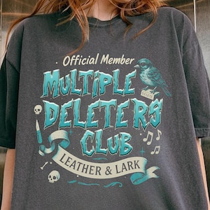 May include: A dark gray t-shirt with a blue and white graphic design that says "Official Member Multiple Deleters Club Leather & Lark".