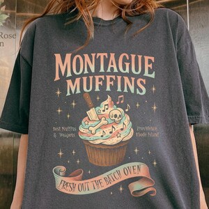 May include: Dark gray t-shirt with the text "MONTAGUE MUFFINS" and a cupcake graphic. The cupcake has a skull and crossbones design with a knife and musical notes. The shirt also has the text "Best Nuffins & Weapons" and "Fresh Out The Batch Oven".