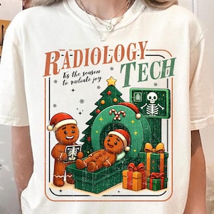 Puede incluir: Camiseta color crema con un diseño festivo. El gráfico presenta hombres de jengibre con gorros de Papá Noel, un árbol de Navidad y una máquina de imágenes médicas. El texto dice "Radiology Tech" y "Tis the season to radiate joy."