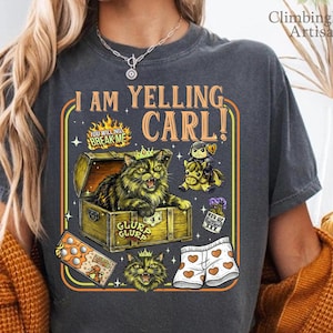 May include: Dark gray t-shirt with a graphic that says "I AM YELLING CARL!". The graphic features a cat in a treasure chest, a knight on a horse, and other cartoon elements. The shirt has a vintage, worn look.