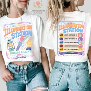 Pu&ograve; includere: Magliette bianche con grafica colorata. Una maglietta presenta "VBS 2026 ILLUMINATION STATION" con una lanterna, una torcia e una lampadina. L'altra maglietta ha "ILLUMINATION STATION" e un elenco di versetti biblici. Entrambe le magliette hanno il testo "Shining a light on who Jesus really is."