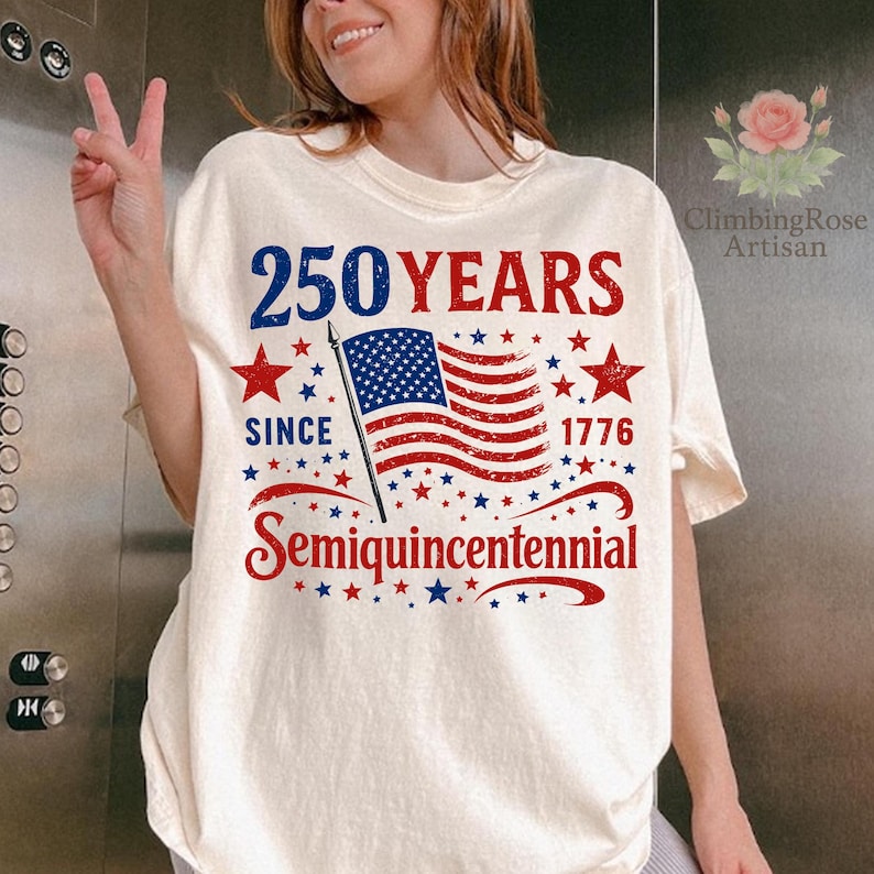May include: Cream-colored t-shirt with a patriotic design celebrating 250 years since 1776. The design features the text "250 YEARS" in blue and red, an American flag, stars, and the word "Semiquincentennial".
